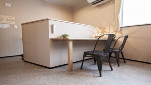 Ein kompakter Arbeitsraum mit Schreibtisch, zwei Stühlen, einer kleinen Pflanze und einem Fenster mit Vorhängen.