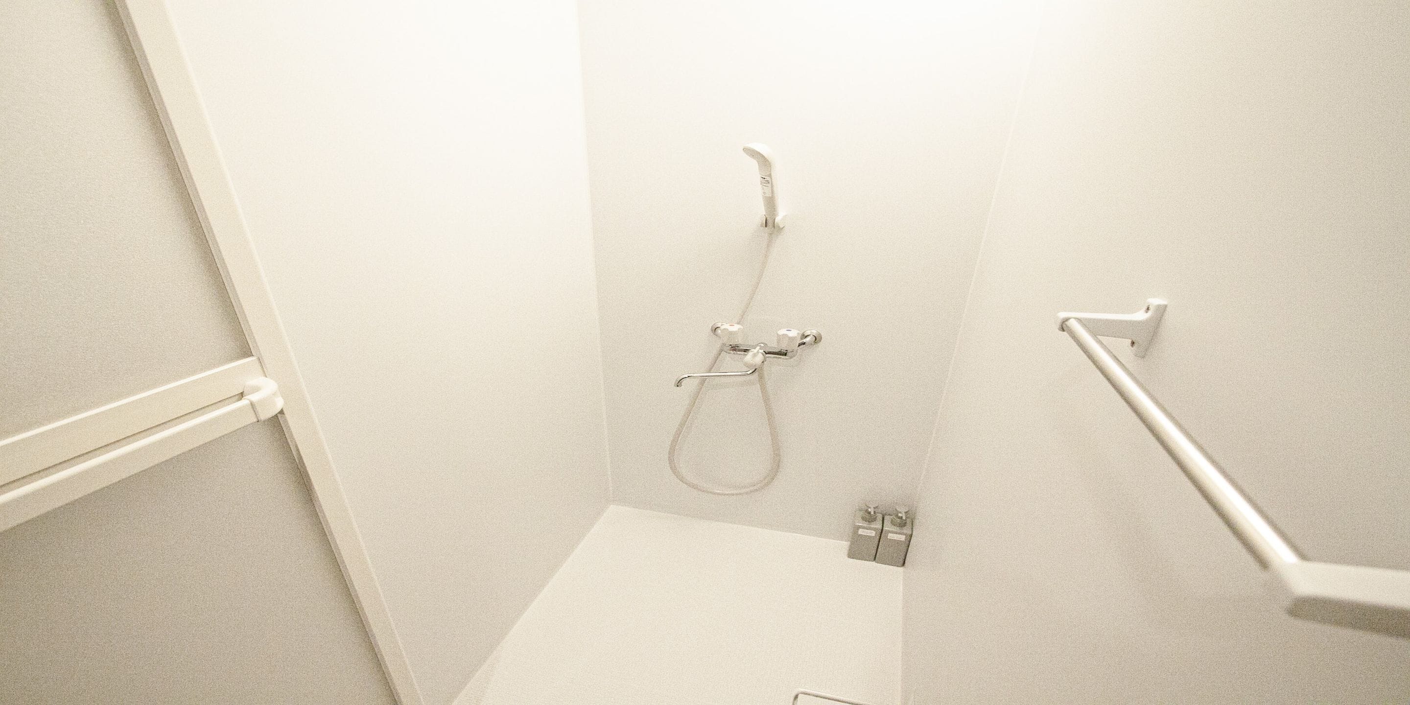 A small, white bathroom with a shower, a toilet, and a handrail.