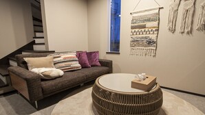 Ein modernes Wohnzimmer mit einer Couch, Kissen, einem runden Korbtisch und einer Wanddekoration aus Makramee.