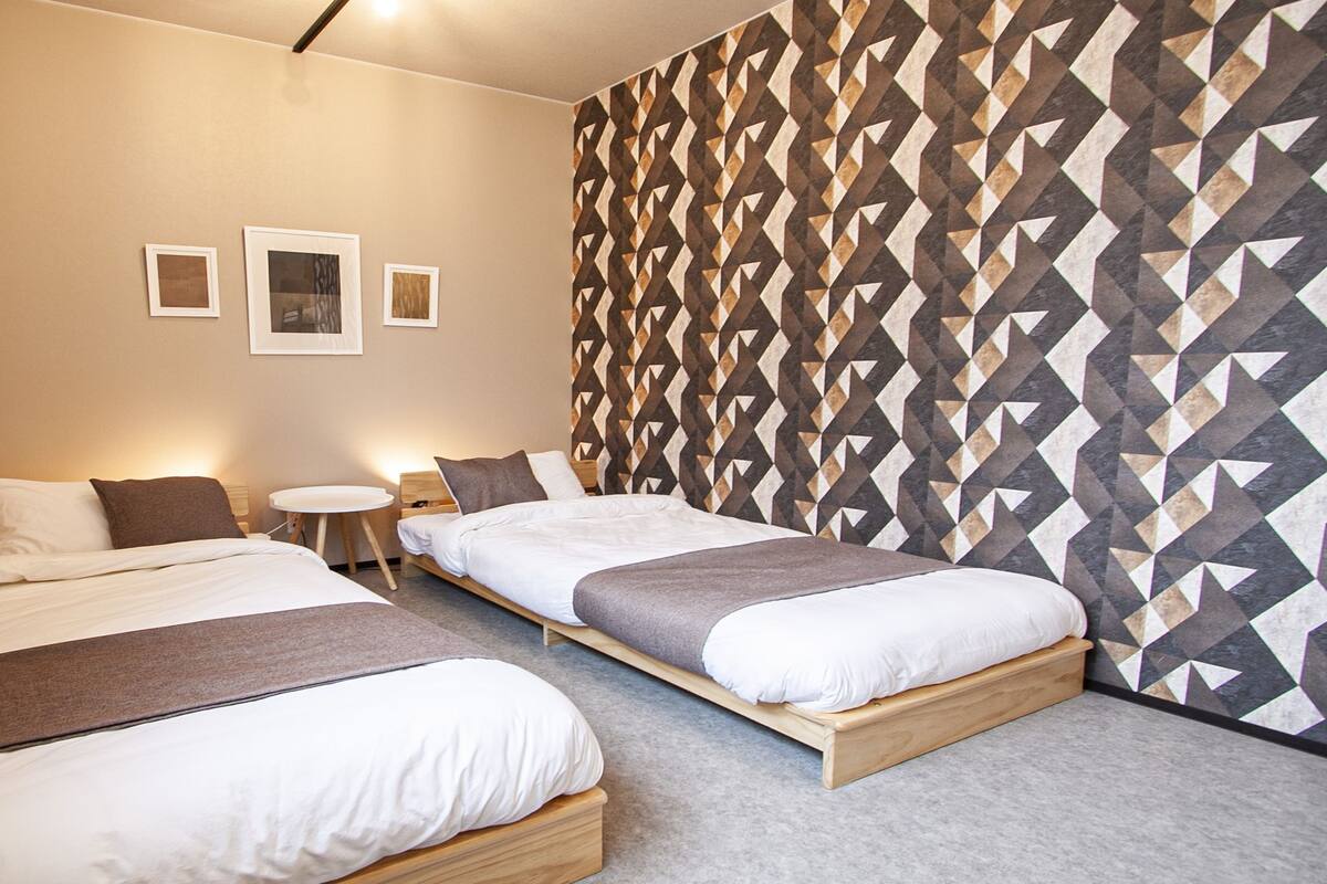 A hotel room with two beds, a small round table, and a geometric patterned wall.