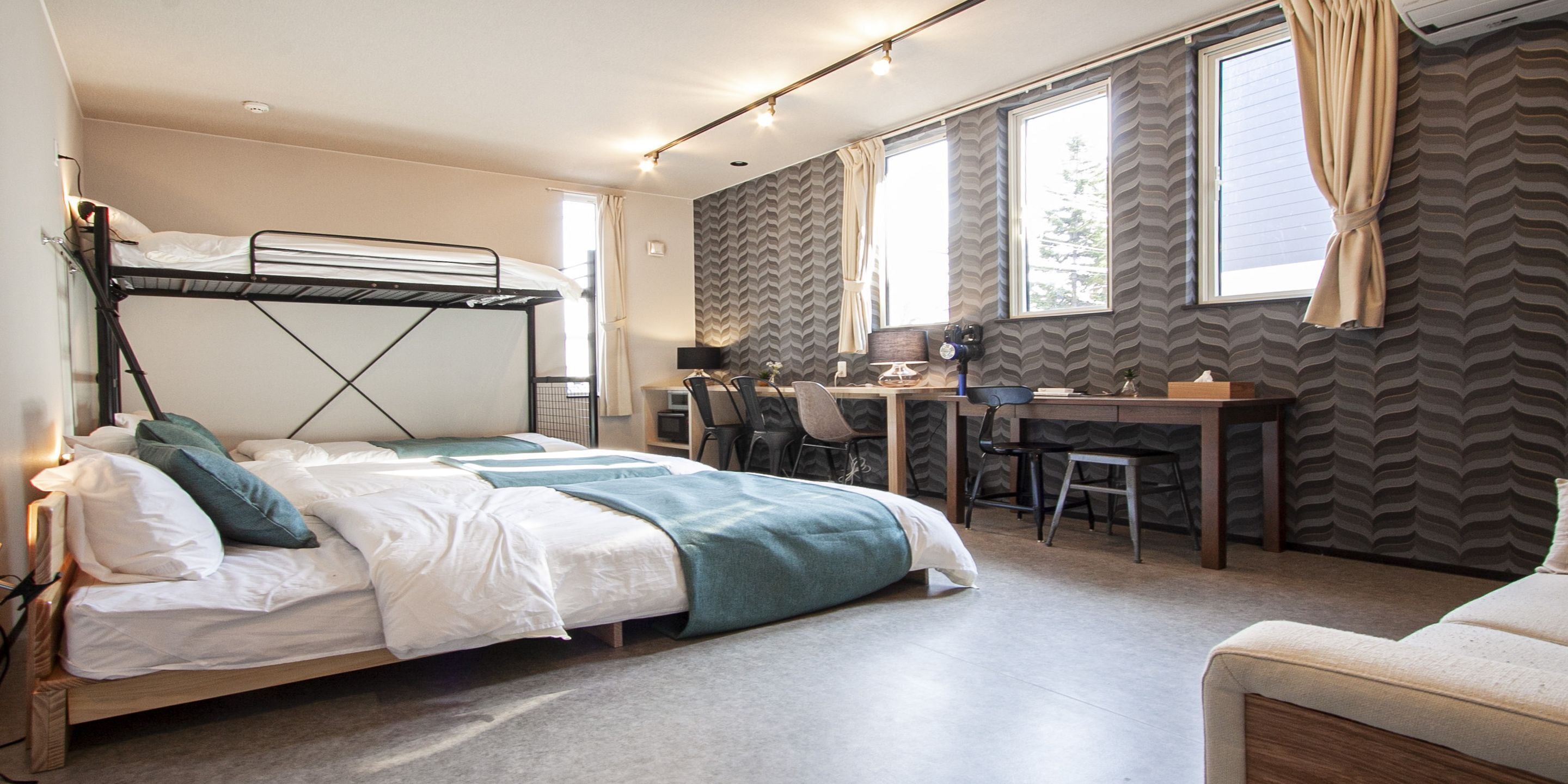 A bunk bed with a desk and chair, a sofa, and a window with curtains.
