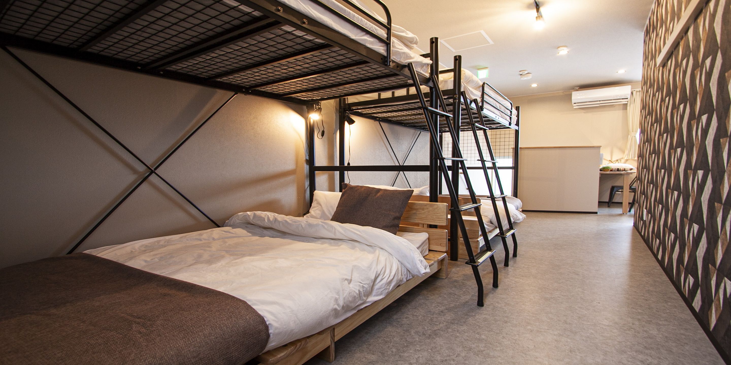 A bunk bed room with a wooden ladder, a desk, and a patterned wall.