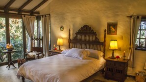 Ein Schlafzimmer mit einem großen Bett, zwei Nachttischen mit Lampen, einem kleinen Tisch mit Kerzen und Blick ins Grüne.
