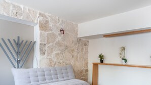 A room with a stone wall, a sofa, a small table, and a wooden shelf with plants. - Hotel Rimon (Cozumel)