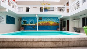 A swimming pool with a mural of a sunset over water, a balcony with white railings, and a sign indicating a no swimming zone. - Hotel Rimon (Cozumel)