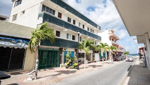 A multi-story hotel with a balcony on the second floor, a gated entrance, and a street view with parked vehicles and palm trees. - Hotel Rimon (Cozumel)