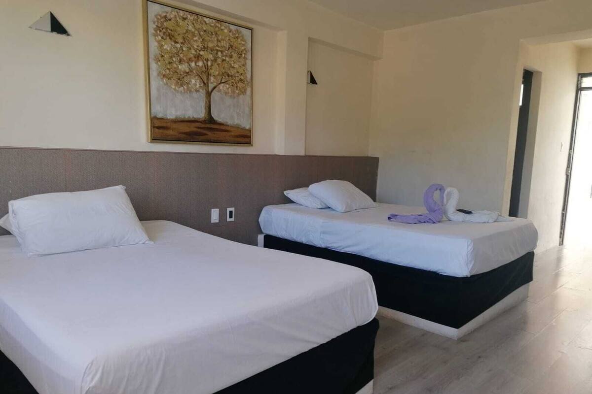 A hotel room with two beds, a painting of a tree, and a wooden floor.