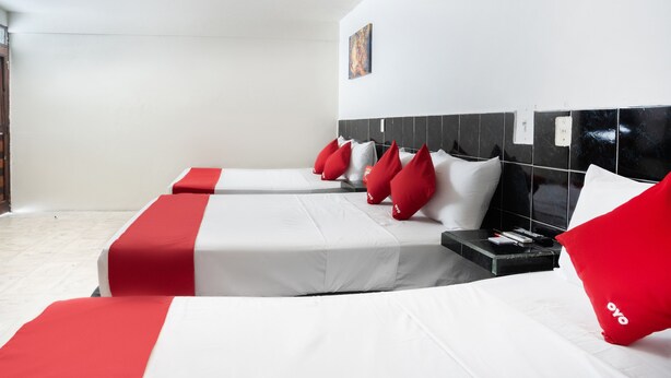 A hotel room with two beds, each with white bedding and red accents, a black headboard, and a small bedside table with a lamp. - Hotel Rimon (Cozumel)