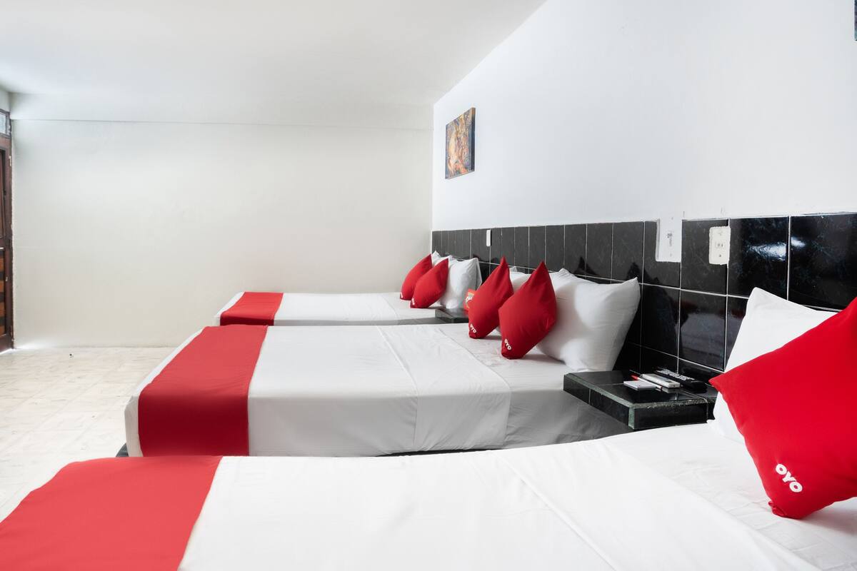 A hotel room with two beds, each with white bedding and red accents, a black headboard, and a small bedside table with a lamp.