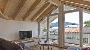 A modern living room with a large window, a flat-screen TV, and a sofa.