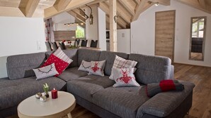 A modern living room with a grey sectional sofa, a round wooden coffee table, and a kitchen in the background.