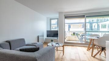 A modern living room with a grey sofa, a small round table with a cactus, and a TV on a stand.