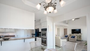 Una cocina moderna con armarios blancos, una mesa de comedor de vidrio y una araña.