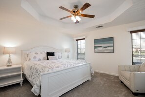 Une chambre à coucher comprenant un lit, un ventilateur de plafond, une table de chevet, une chaise et une fenêtre avec des stores.