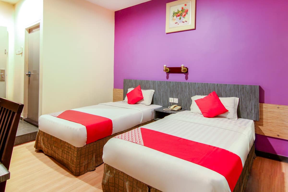 Habitación de hotel con dos camas, cada una con cubrecama rojo y blanco, cabeceros de madera y una pared de acento morada.