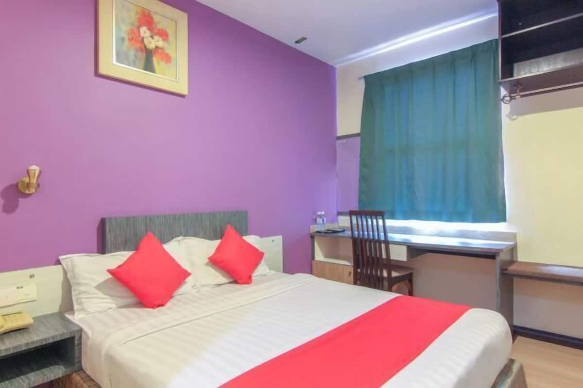 Habitación de hotel con cama, escritorio, silla, ventana con cortinas y un cuadro en la pared.