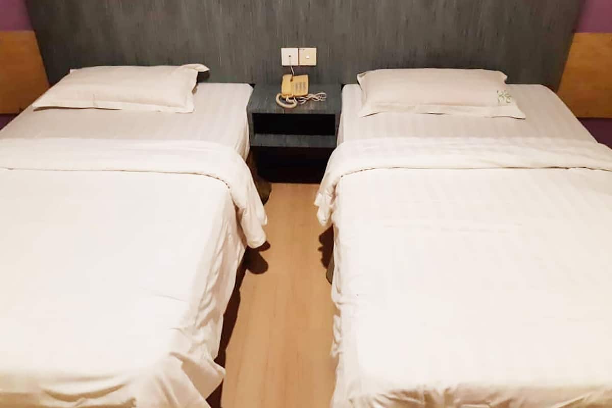 Una habitación con dos camas individuales, una mesita con un teléfono y un interruptor de luz en la pared.
