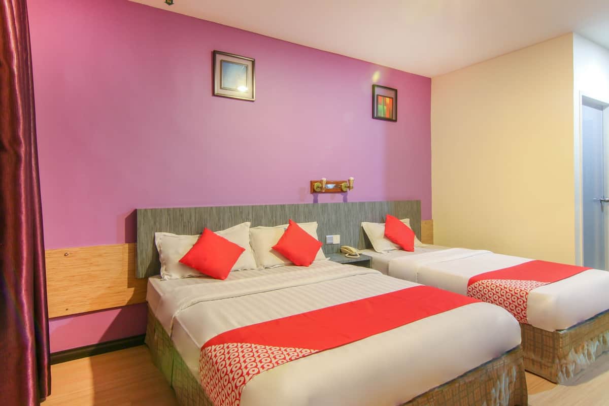 Habitación de hotel con dos camas, cada una con ropa blanca y detalles rojos, cabeceros de madera y una mesita de noche pequeña con una lámpara.