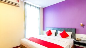 Una habitación de hotel con cama, mesita de noche con teléfono y ventana con cortinas.