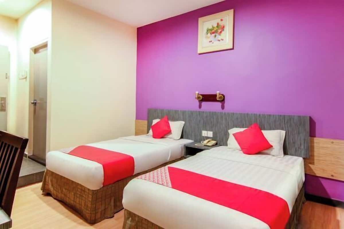 Habitación de hotel con dos camas, una silla de madera, una mesita pequeña y una pared morada.