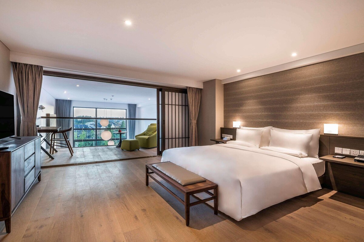 Ein modernes Hotelzimmer mit einem großen Bett, einem Schreibtisch und einem Balkon mit Aussicht.