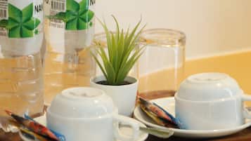 Een gedekte tafel met witte kopjes en schoteltjes, een kleine potplant en een glas water.