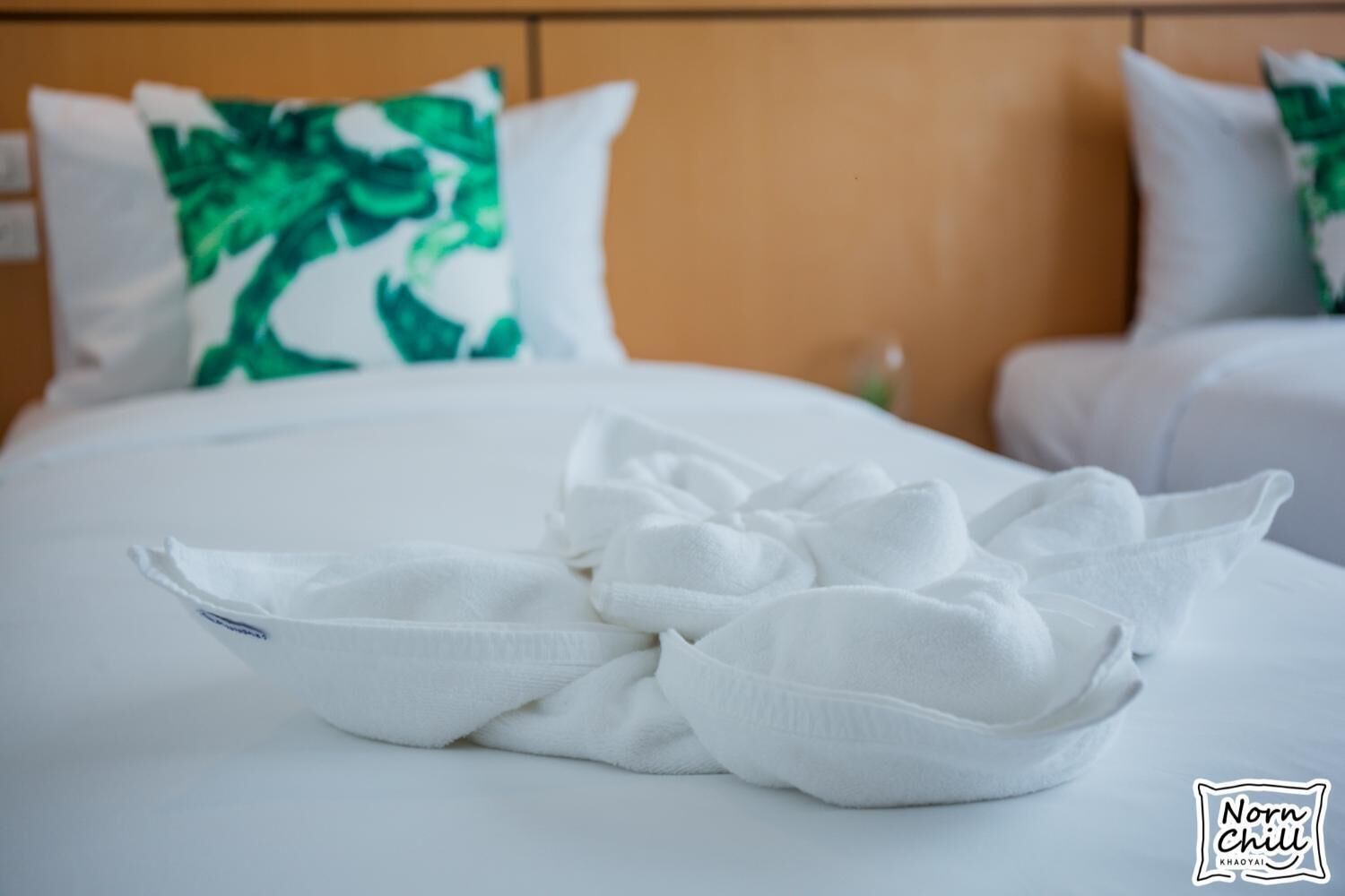 A neatly made bed with white linens and a folded towel in the center.