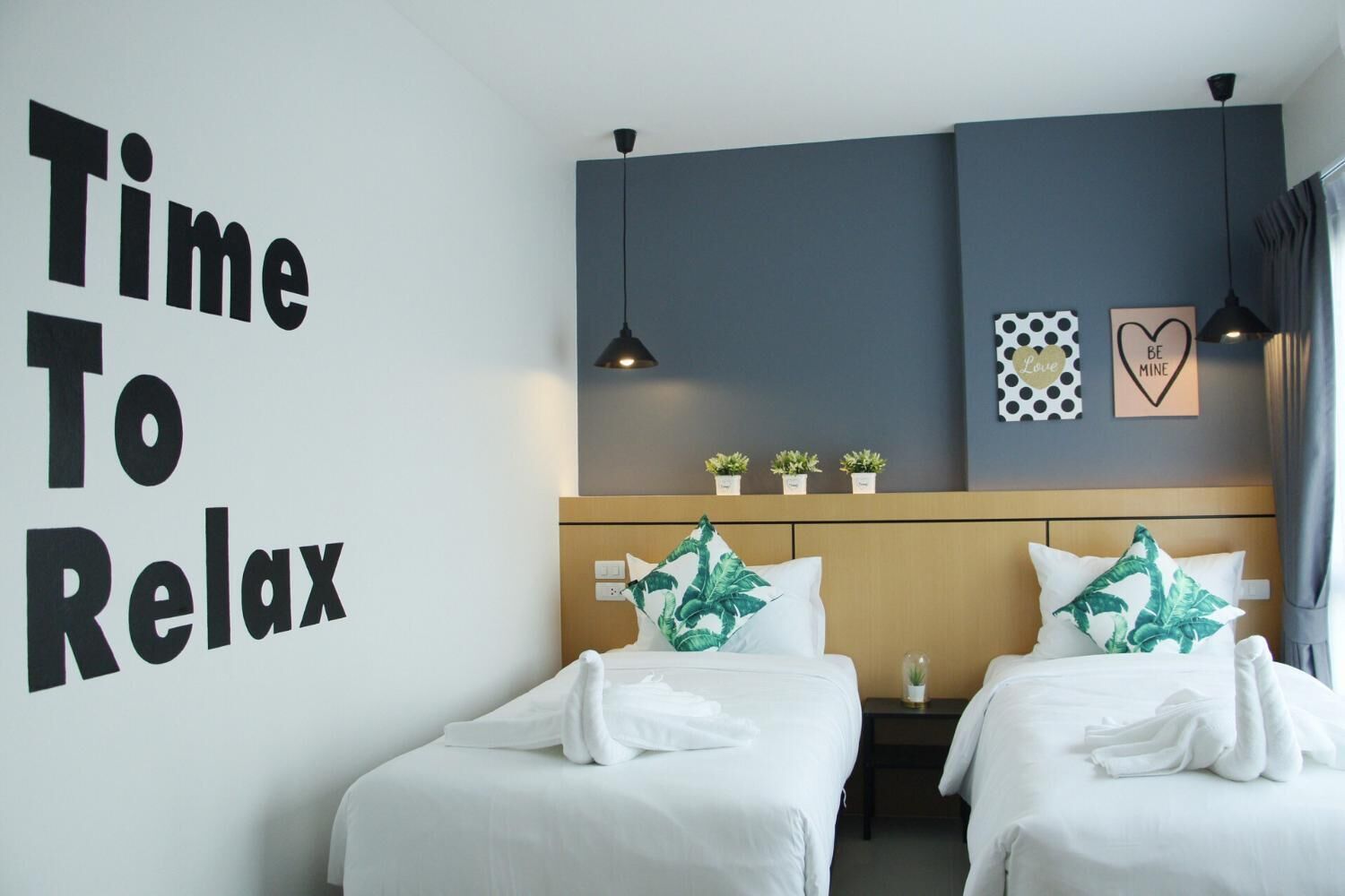 Une chambre d’hôtel avec deux lits, un mur orné de l’inscription « Il est temps de se détendre » et un tableau encadré représentant un cœur.