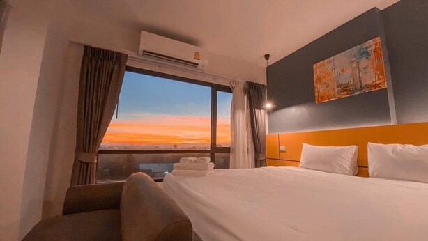 Ein Hotelzimmer mit einem großen Bett, einem Kopfteil, einem Gemälde an der Wand und einem Fenster mit Vorhängen.