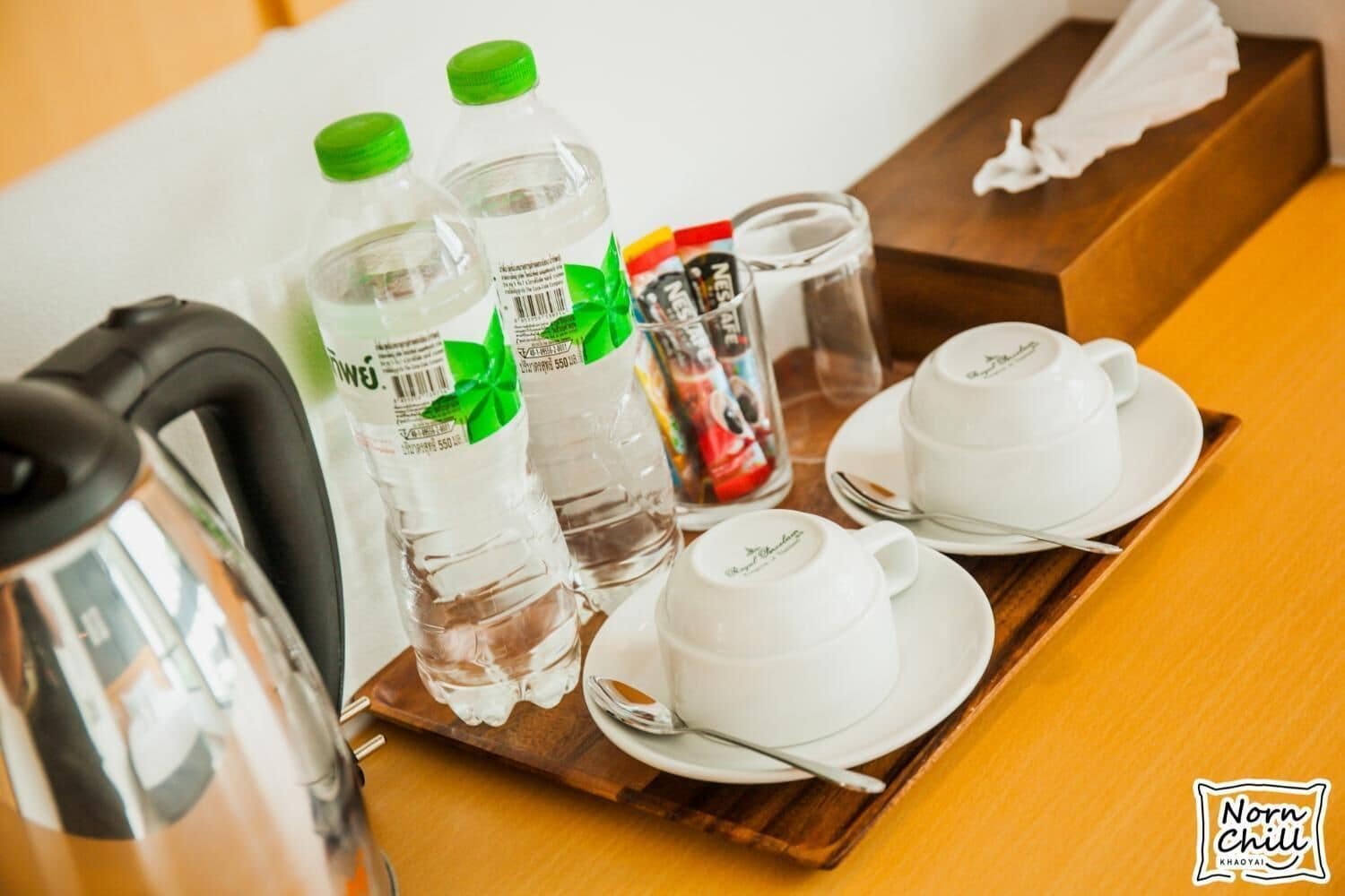 A tray with water bottles, a glass, a teapot, and teacups on a wooden table.