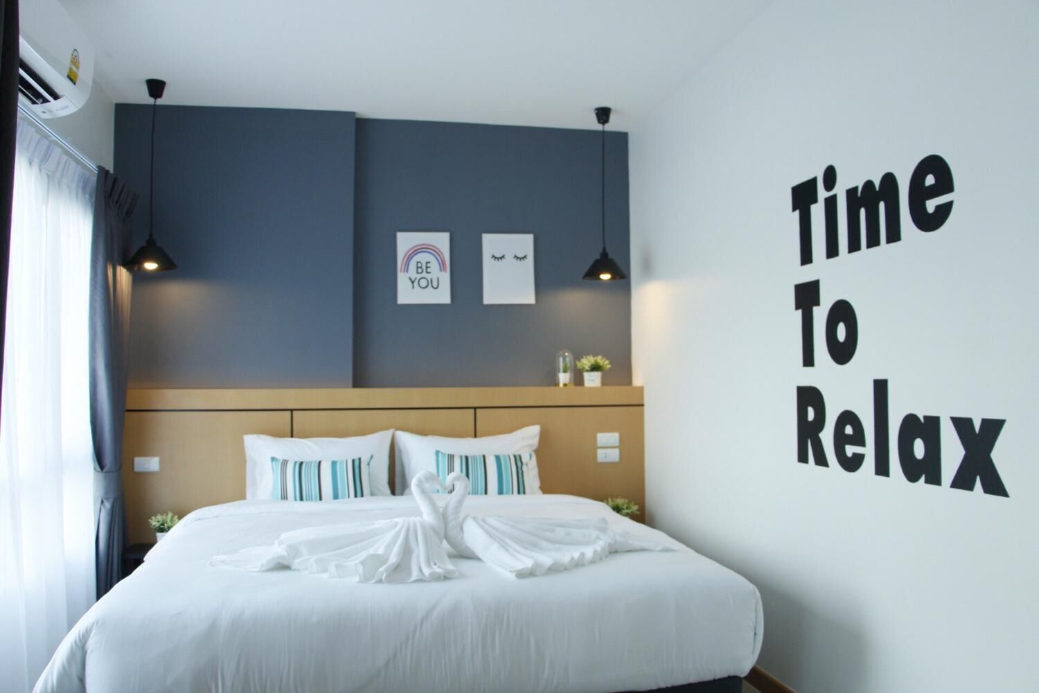 Una habitación de hotel con una cama, una pared con el texto "Time To Relax" y dos lámparas colgantes.