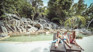 A pool area with lounge chairs, a pool, and surrounding rocks and trees. - Aman Tioman Beach Resort (Tioman Island)