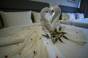 A hotel room with a neatly made bed featuring a decorative swan towel arrangement and a small plant with red petals. - Aman Tioman Beach Resort (Tioman Island)