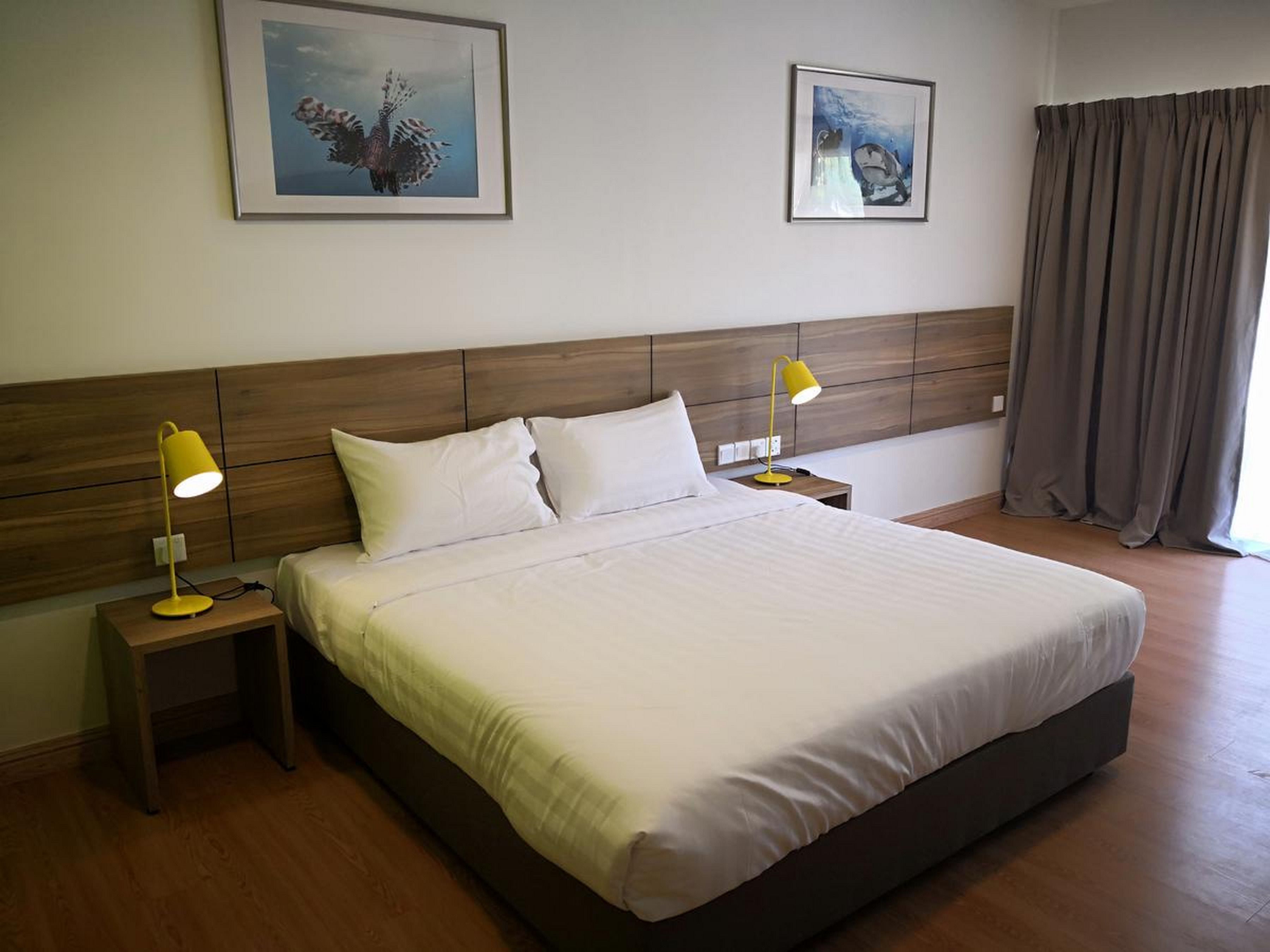 Una habitación de hotel con una cama grande, dos mesitas de noche con lámparas, un cabecero de madera y dos cuadros enmarcados en la pared.
