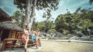 A wooden bench with two people sitting, surrounded by a tropical garden with large rocks and trees. - Aman Tioman Beach Resort (Tioman Island)