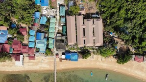 An aerial view of a coastal area with a pier extending into turquoise waters, surrounded by buildings with varied roof colors. - Aman Tioman Beach Resort (Tioman Island)