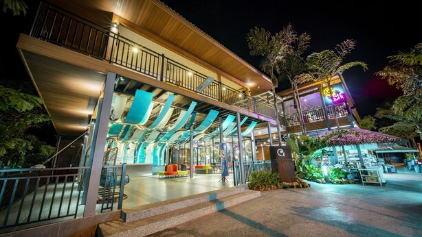 A multi-level building with a covered entrance, outdoor seating area, and a neon sign. - Aman Tioman Beach Resort (Tioman Island)