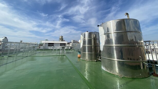 A rooftop with large cylindrical tanks, a green roof, and a clear sky. - Guesthouse Base Okinawa - Hostel (Naha)