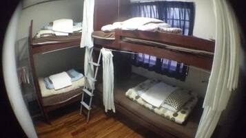 A bunk bed room with a ladder, a window with curtains, and a wooden floor.