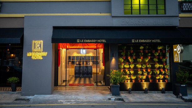 La façade de l’hôtel Le Embassy, avec son entrée, une enseigne et une rangée de plantes en pot.