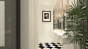 Un couloir avec un sol à carreaux noirs et blancs, un tableau encadré au mur et une plante sur la droite.