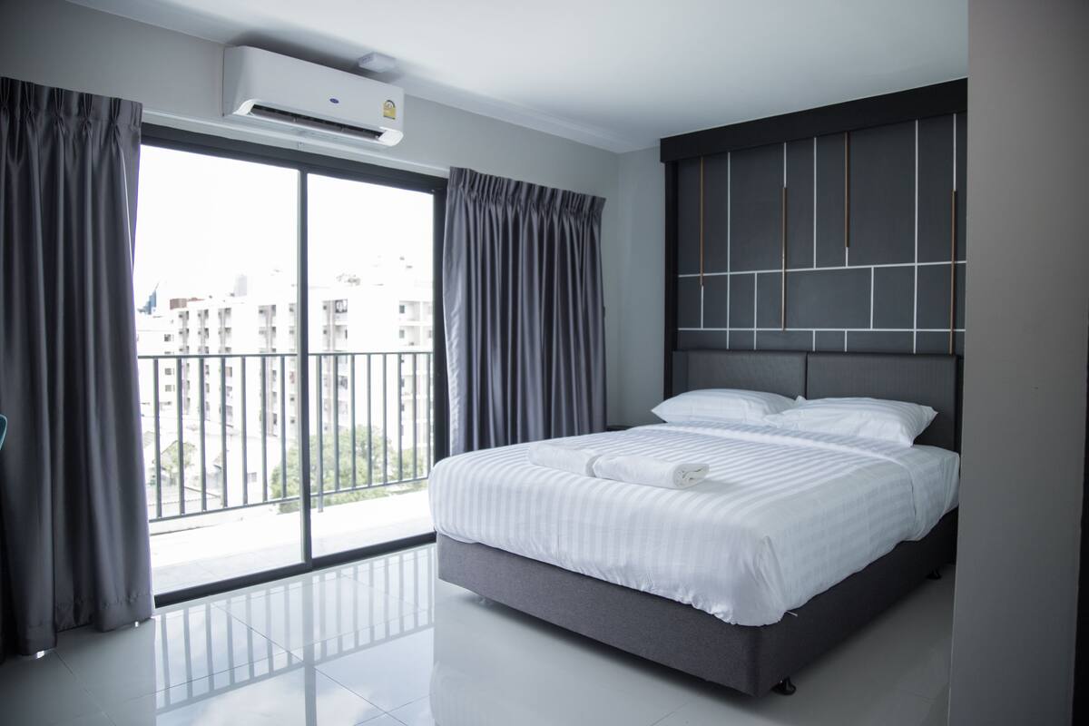 Une chambre d’hôtel moderne avec un grand lit, un balcon doté de rideaux et une vue sur la ville.