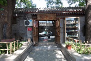 A traditional Chinese gate with a wooden door and a tiled roof, leading to a courtyard with potted plants and a car parked inside.