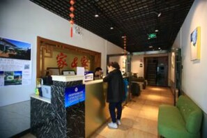 A reception area with a marble counter, a green seating area, and a ceiling with visible beams and hanging decorations. - Beijing Xingshe Hotel (Beijing)