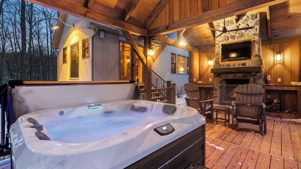 A wooden deck with a hot tub, stone fireplace, and outdoor seating.