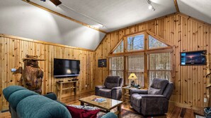A cozy living room with wooden walls, a television, two armchairs, a coffee table, and a fireplace.