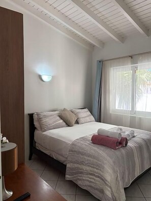 A hotel room with a bed, a bedside table, a lamp, and a window with curtains.