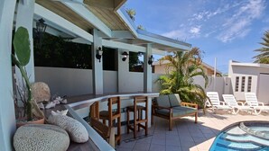 A covered outdoor area with a pool, lounge chairs, and a seating arrangement. - Palm Beach Vacation Villa (Noord)