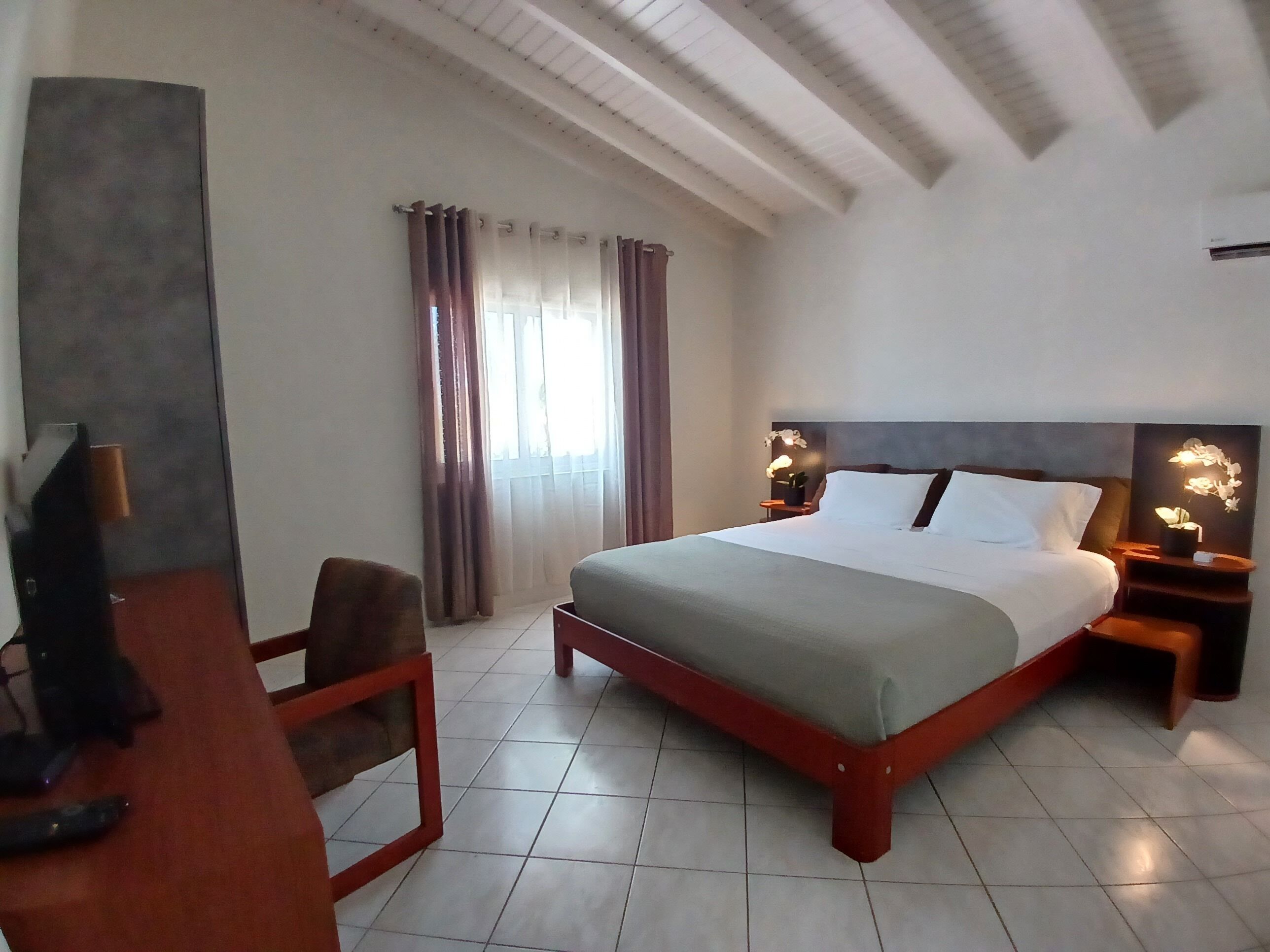 Hotelkamer met een groot bed, een bureau met stoel, een televisie en een raam met gordijnen.