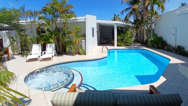A swimming pool with a hot tub, surrounded by palm trees and lounge chairs. - Palm Beach Vacation Villa (Noord)
